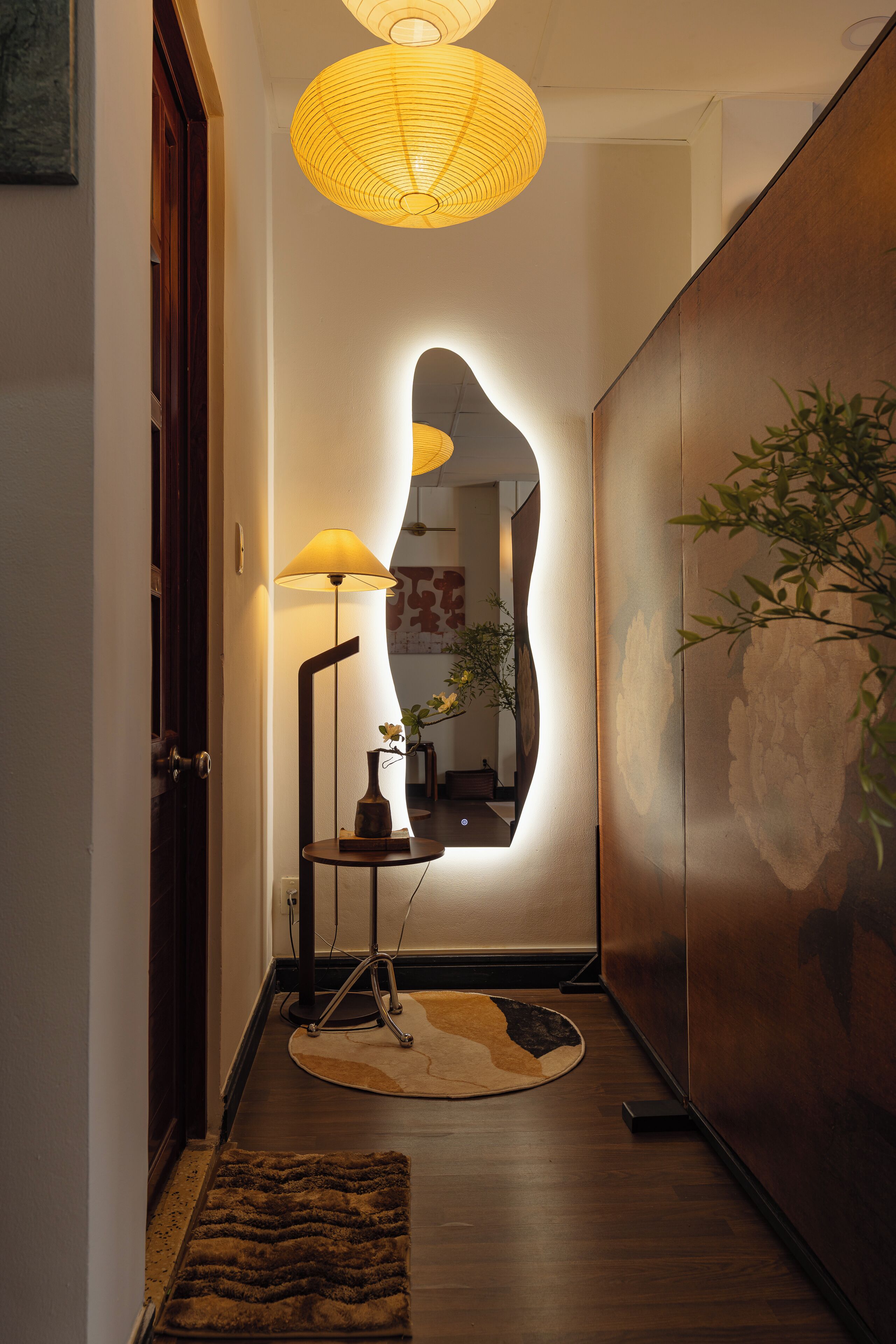 Un couloir avec une table ronde, une lampe et un miroir.