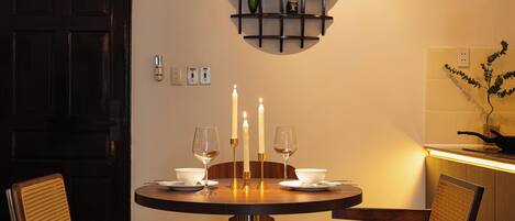 Een eethoek met een ronde tafel, stoelen en een wandplank met decoratieve objecten.