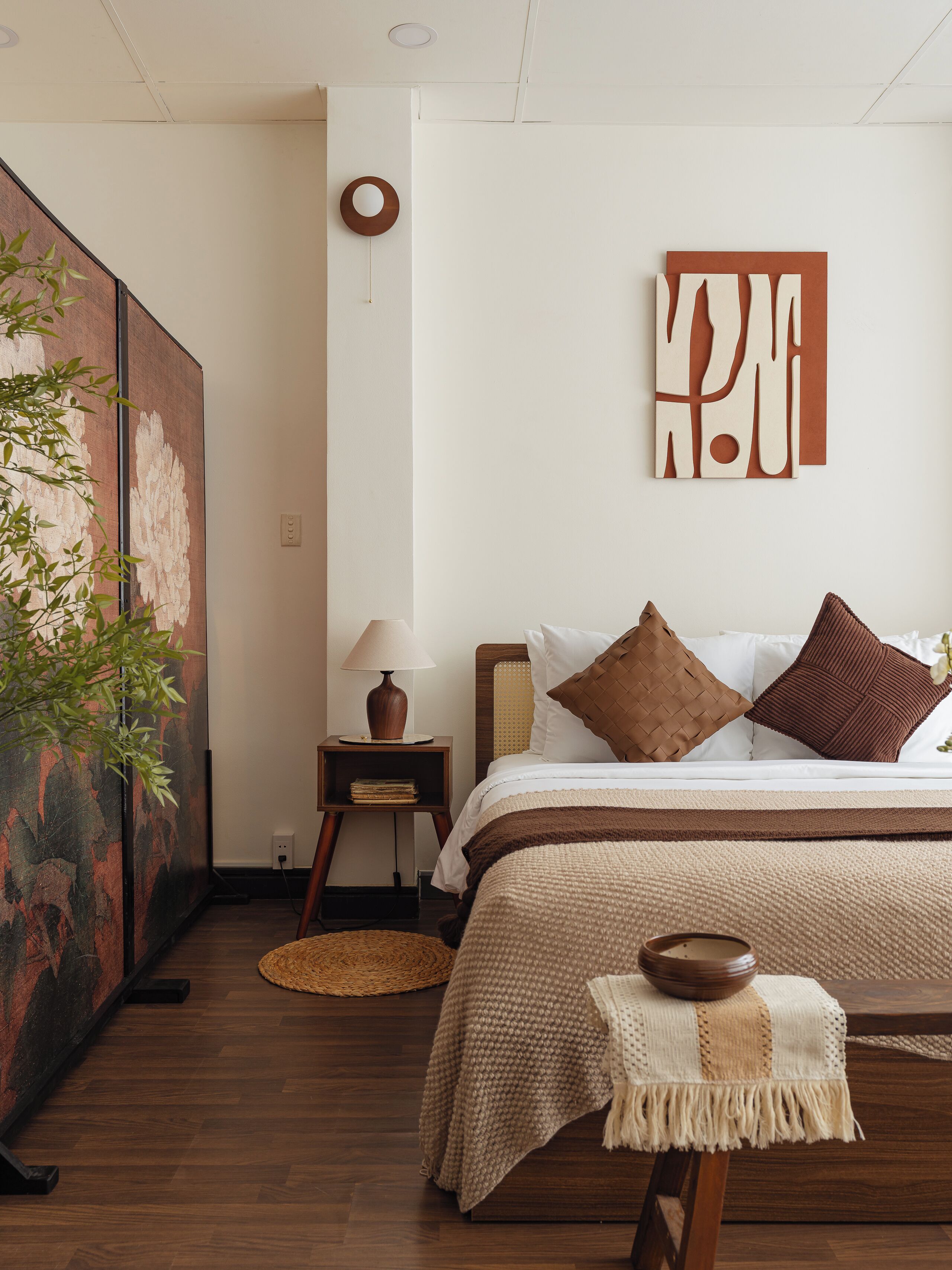 Un dormitorio con cama, almohadas, mesita de noche, lámpara, una obra de arte en la pared y un cuadro grande.