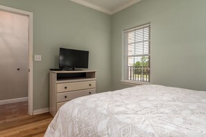 Ein Schlafzimmer mit einem Bett, einem Fernseher auf einer Kommode, einem Fenster mit Jalousien und einer Tür.