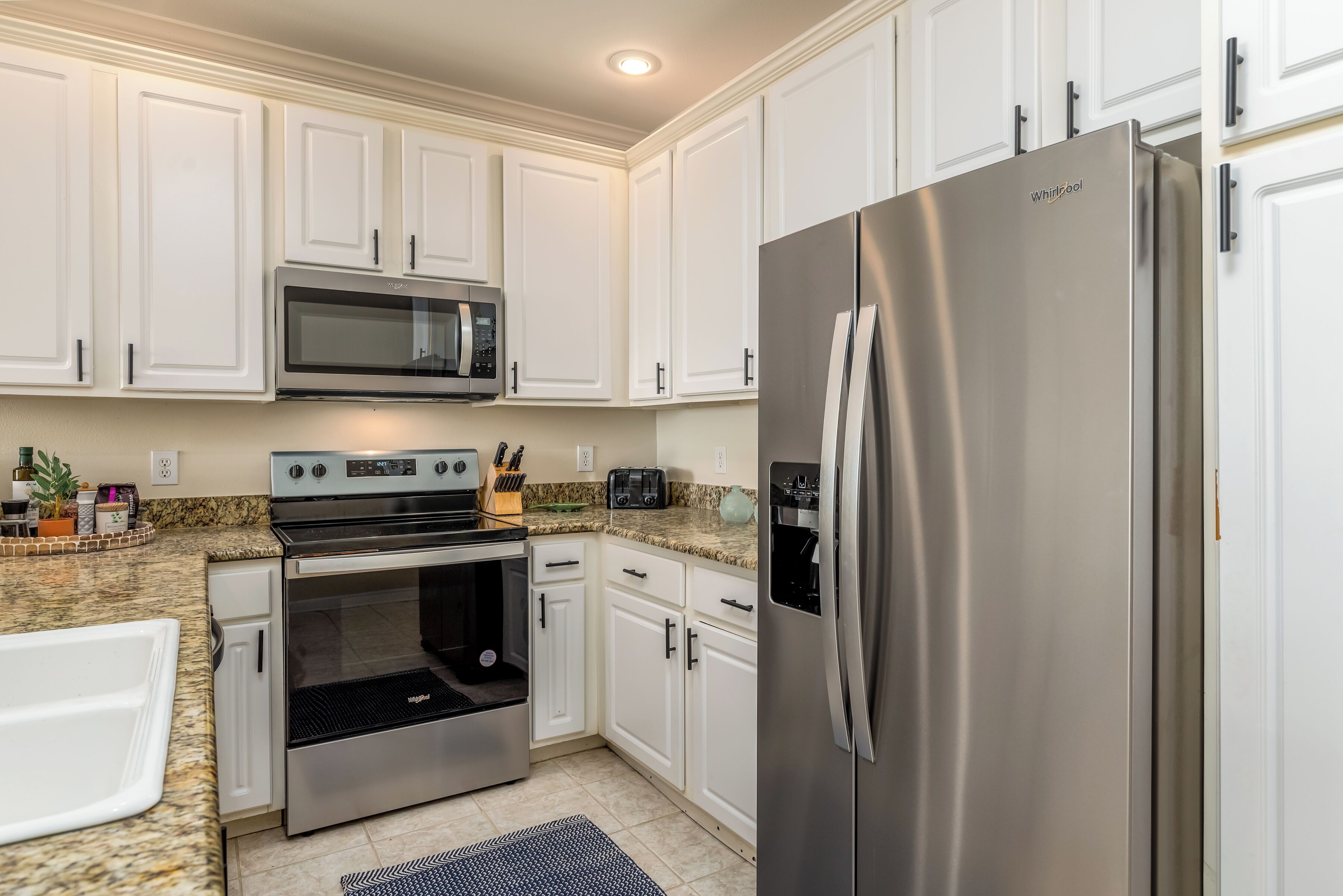 A kitchen with white cabinets, a stainless steel refrigerator, a microwave, an oven, and a toaster.