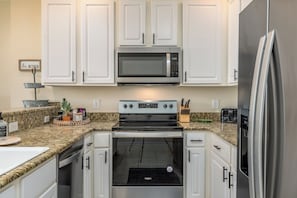 A kitchen with white cabinets, a stainless steel microwave, a built-in oven, and a refrigerator. - Side by Side Beach Condos | Sleeps 18, Pools + Beach Access (Dauphin Island)