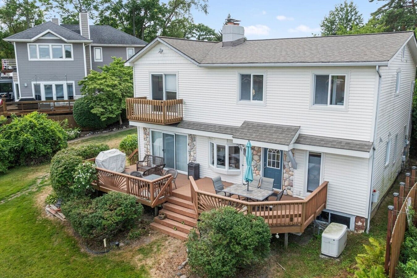 A two-story house with a deck, outdoor seating, and a stone facade.
