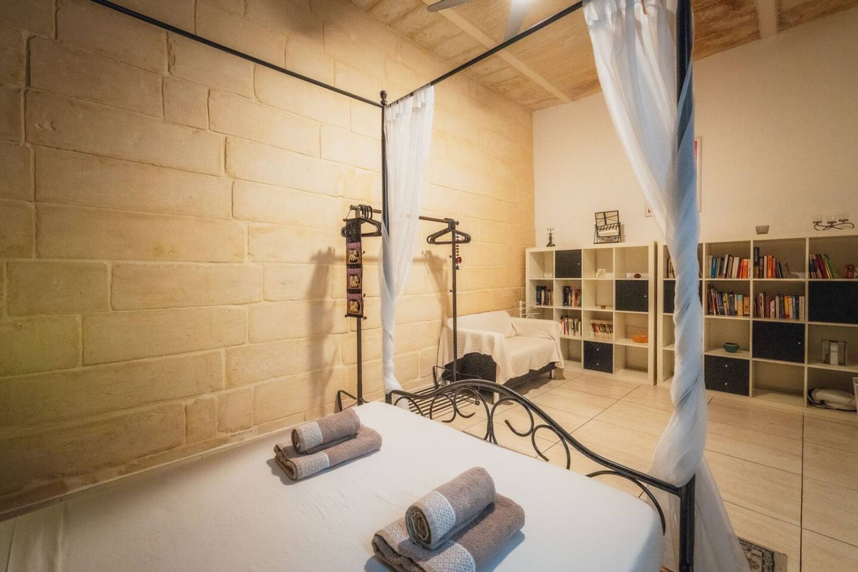 A room with a bed, a bedside table, a bookshelf, and a curtain.