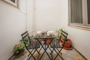A small outdoor patio with a table set for two, surrounded by potted plants and a window. - Casa Due Balli 400-year Historic Valletta House (Valletta)