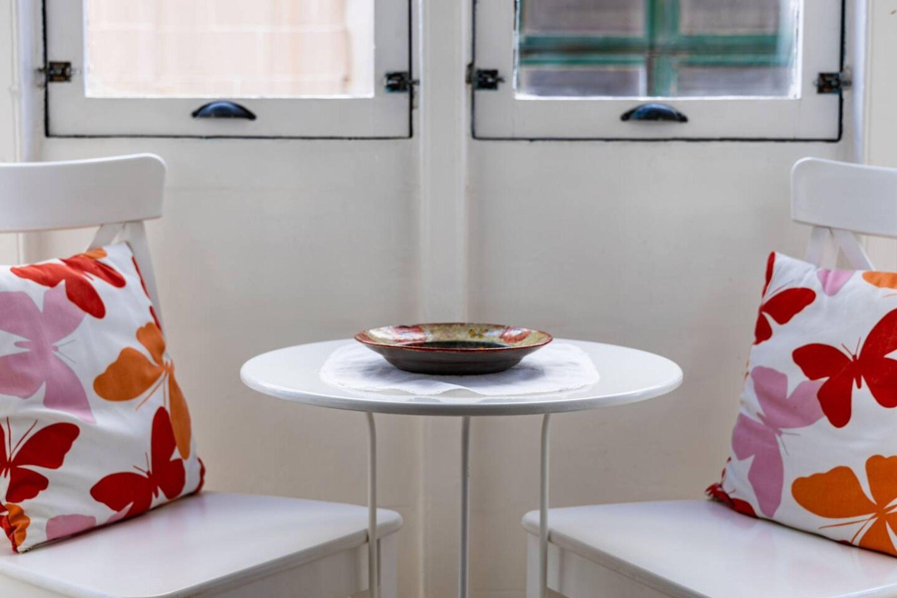 A small table with a bowl on it, flanked by two chairs with floral cushions.