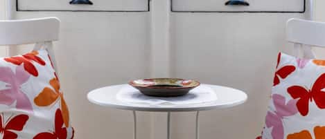 Una pequeña mesa con un tazón, acompañada por dos sillas con cojines estampados.