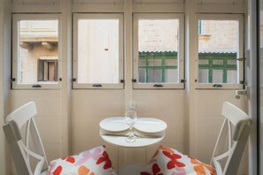 A room with a table and chairs, a window with a view of a building, and a door with a handle. - Casa Due Balli 400-year Historic Valletta House (Valletta)