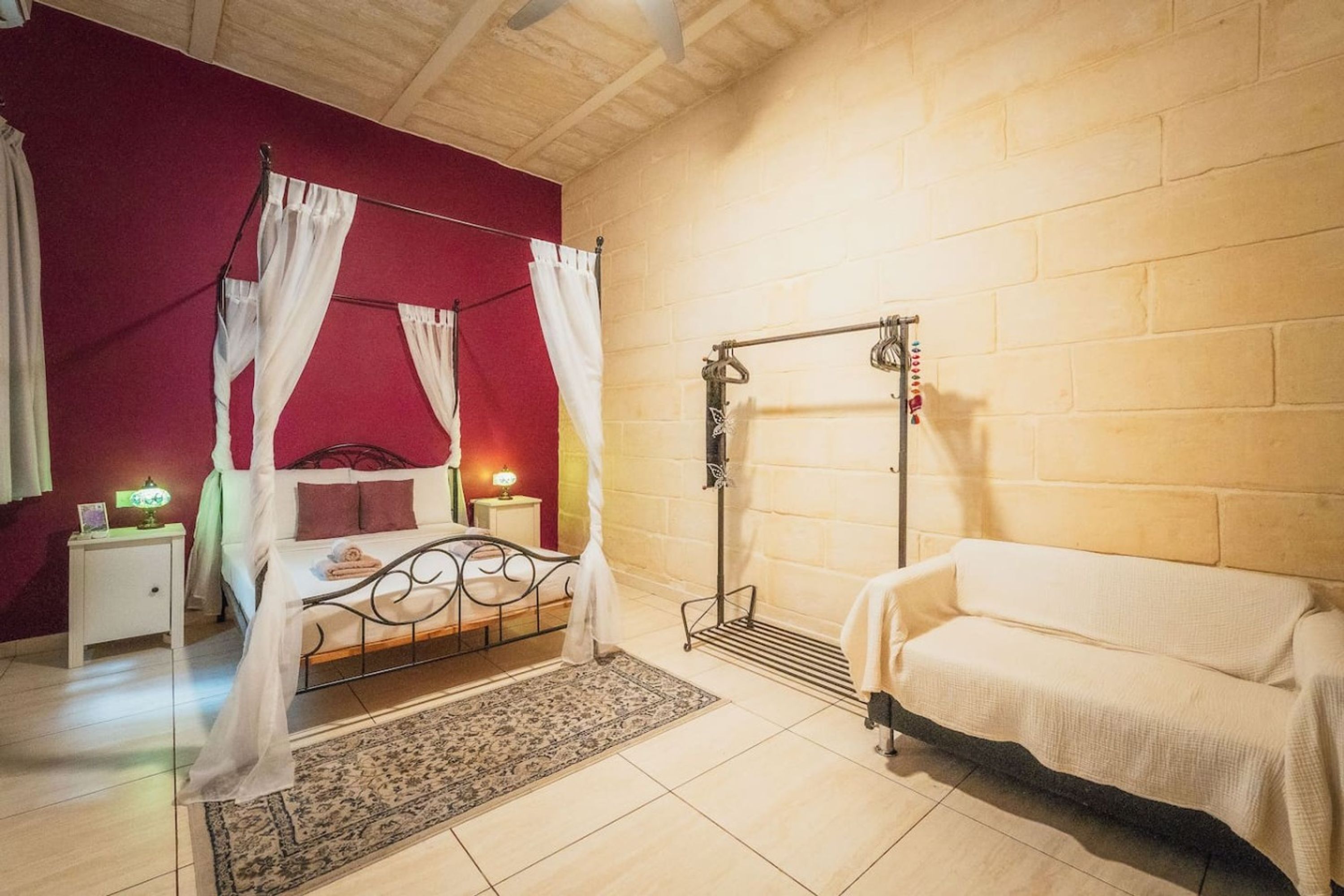 A bedroom with a four-poster bed, a nightstand with a lamp, a bench, and a wall-mounted drying rack.