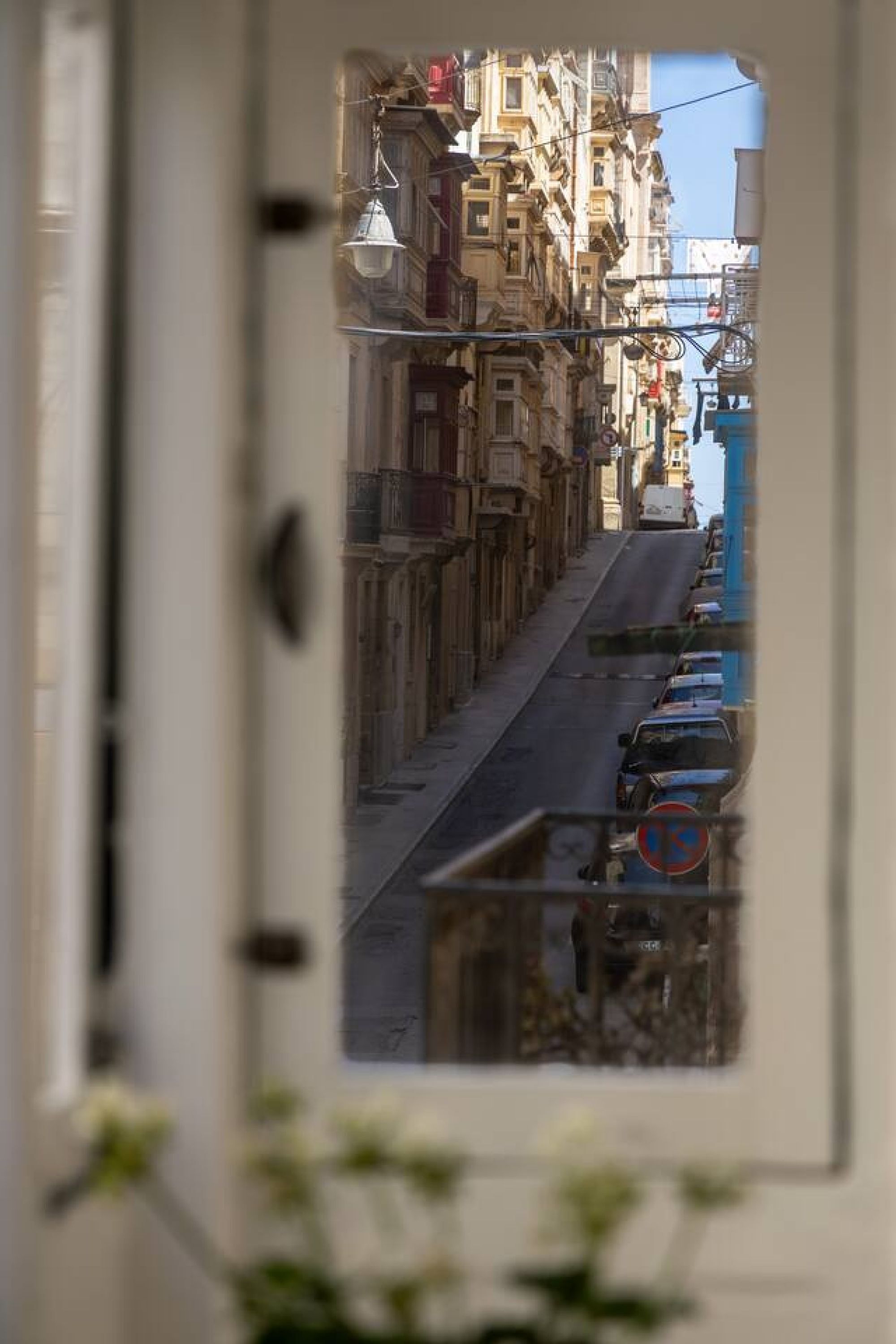 Une rue étroite, bordée de bâtiments des deux côtés, avec une voiture garée et un panneau indiquant qu’il est interdit de se garer.
