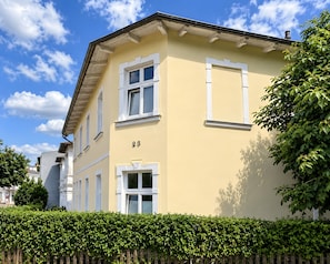A two-story building with a yellow facade, white window frames, and a number '23' on the lower right side. - Ahlbeck 'Agape 2-Room Apartment' for 2 to 4 Guests, 250 m from the Beach (Heringsdorf)