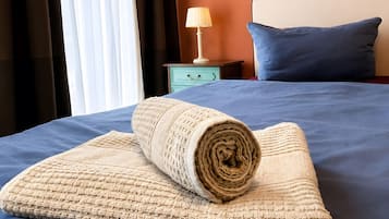 Ein ordentlich bezogenes Bett mit einer zusammengerollten Decke, einer Nachttischlampe und einem blauen Kissen auf einer blauen Bettdecke.