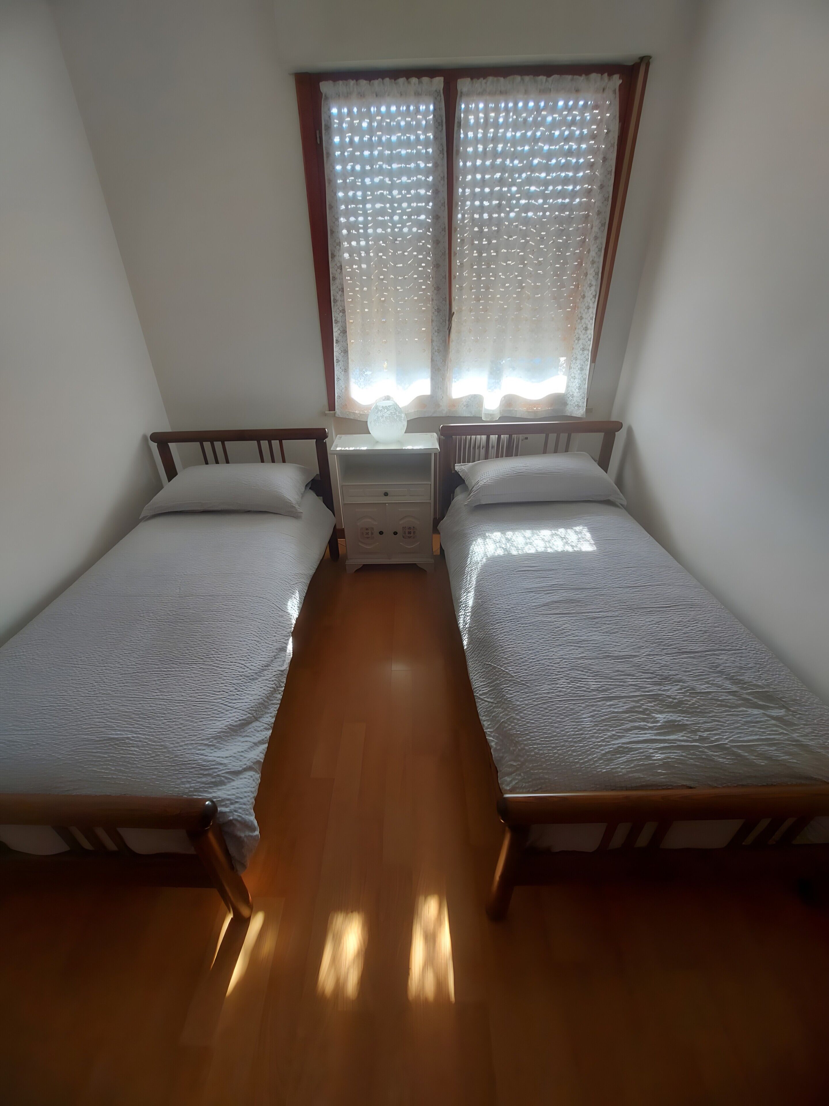 Une chambre avec deux lits simples, une table de chevet avec une lampe et une fenêtre avec des rideaux.