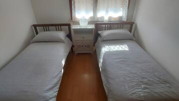 Une chambre avec deux lits simples, une table de chevet avec une lampe et une fenêtre avec des rideaux.