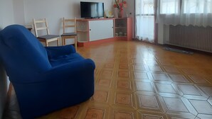 Una sala de estar con un sillón azul, un televisor, un cuadro y una ventana con cortinas.