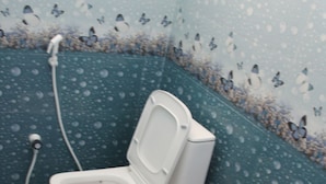 A small, enclosed bathroom with a toilet, a red bidet, and a wall-mounted faucet. - SSV Rooms (Tiruvannamalai)