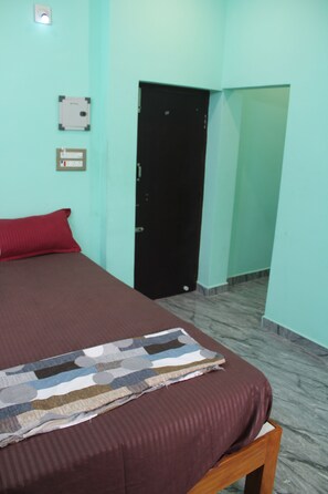 Una habitación con una cama, una puerta y una lámpara fijada a la pared.