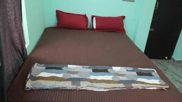 A bed with a brown bedspread, two red pillows, and a patterned blanket. - SSV Rooms (Tiruvannamalai)