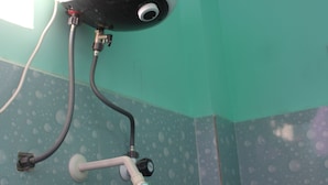 A bathroom with a handheld showerhead mounted on a wall, a hand dryer, and a towel rack. - SSV Rooms (Tiruvannamalai)