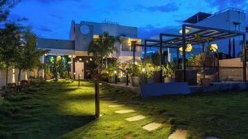 A modern building with a well-maintained garden, a covered outdoor seating area, and a clear sky.