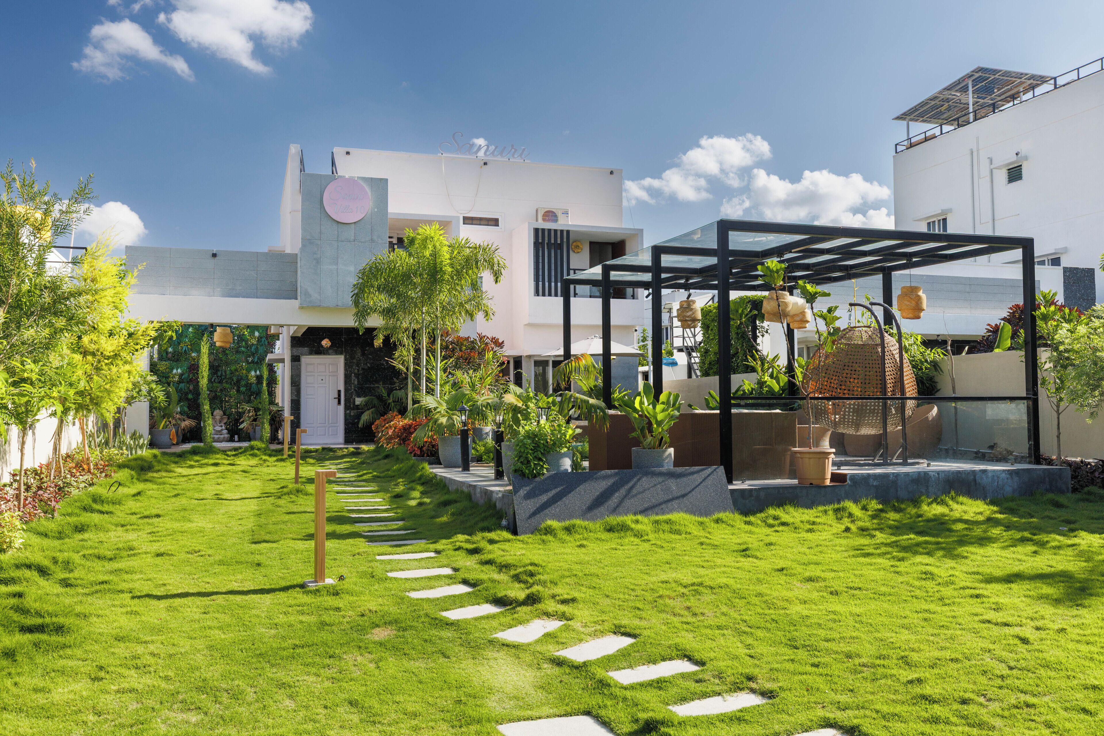 Um edifício moderno com um caminho de jardim que leva a uma área externa coberta e com assentos.