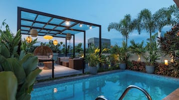 Ett poolområde med en sittgrupp, växter och en pergola med belysning.