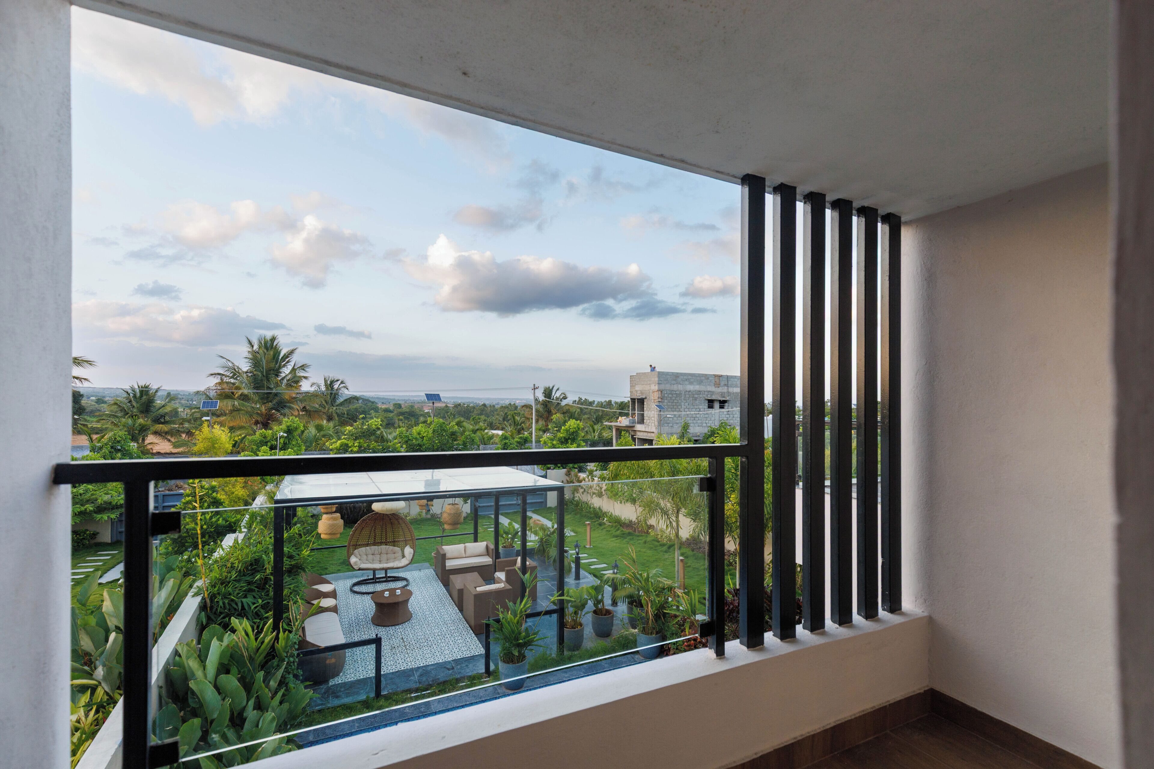 A balcony with a glass railing overlooking a garden and a distant view of the cityscape.