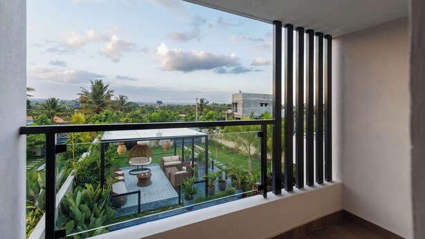 Un balcon doté d’une balustrade en verre, donnant sur un jardin et offrant une vue lointaine sur le paysage urbain.