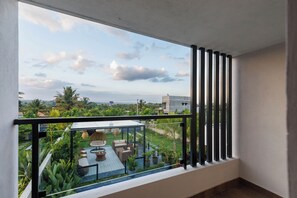 Uma varanda com guarda-corpo de vidro, com vista para um jardim e uma paisagem urbana distante.