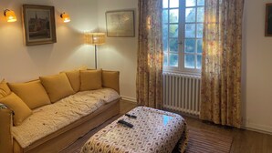 Um quarto com um sofá, uma luminária, uma janela com cortinas e um radiador.