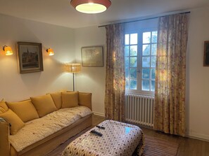 Ein Zimmer mit einer Couch, einer Lampe, einem Fenster mit Vorhängen und einer Heizung.