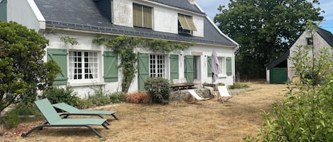 A house with a sloped roof, a front porch with a table and chairs, and a small shed in the background.