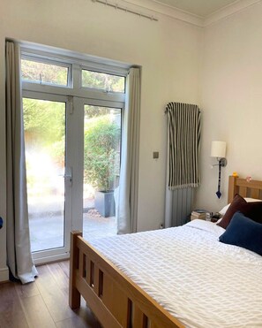 A bedroom with a bed, a nightstand, a lamp, a window with curtains, and a view of greenery outside. - Beautiful and spacious 2 Double Bed, 2 Bath Garden Flat, Ealing, London, W5 (London)