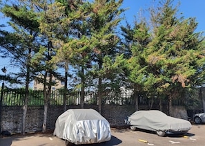 Two covered vehicles parked in a lot with a brick wall and trees in the background. - Beautiful and spacious 2 Double Bed, 2 Bath Garden Flat, Ealing, London, W5 (London)