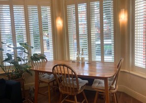 A dining area with a wooden table and chairs, large windows with blinds, and a potted plant. - Beautiful and spacious 2 Double Bed, 2 Bath Garden Flat, Ealing, London, W5 (London)