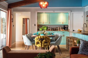Une cuisine moderne avec des meubles de couleur turquoise, un coin repas avec une table ronde et des chaises, et un salon avec un canapé et un coussin à motifs.