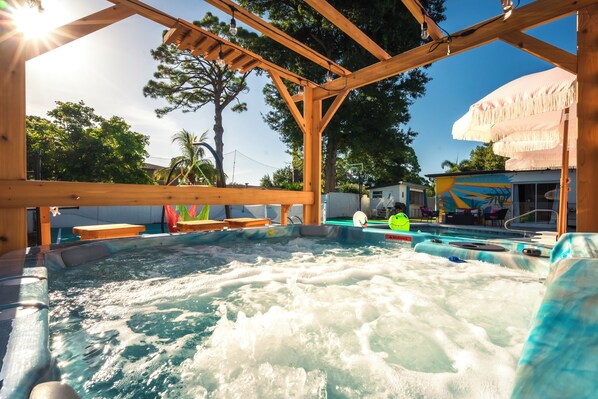Un espace avec un jacuzzi, agrémenté de poutres en bois au-dessus, une piscine avec un panneau de sécurité et une fresque sur le mur du bâtiment.