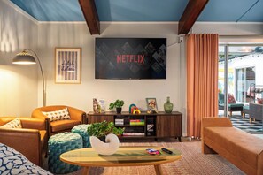 Un salon comprenant un canapé, un fauteuil, une table basse et un téléviseur fixé au mur, sur lequel est affiché le logo « NETFLIX ».