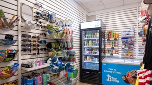 A store with shelves stocked with sunglasses, sunglasses cases, and various other items. - Phoenix Iii 3056 2 Bedroom Condo (Orange Beach)