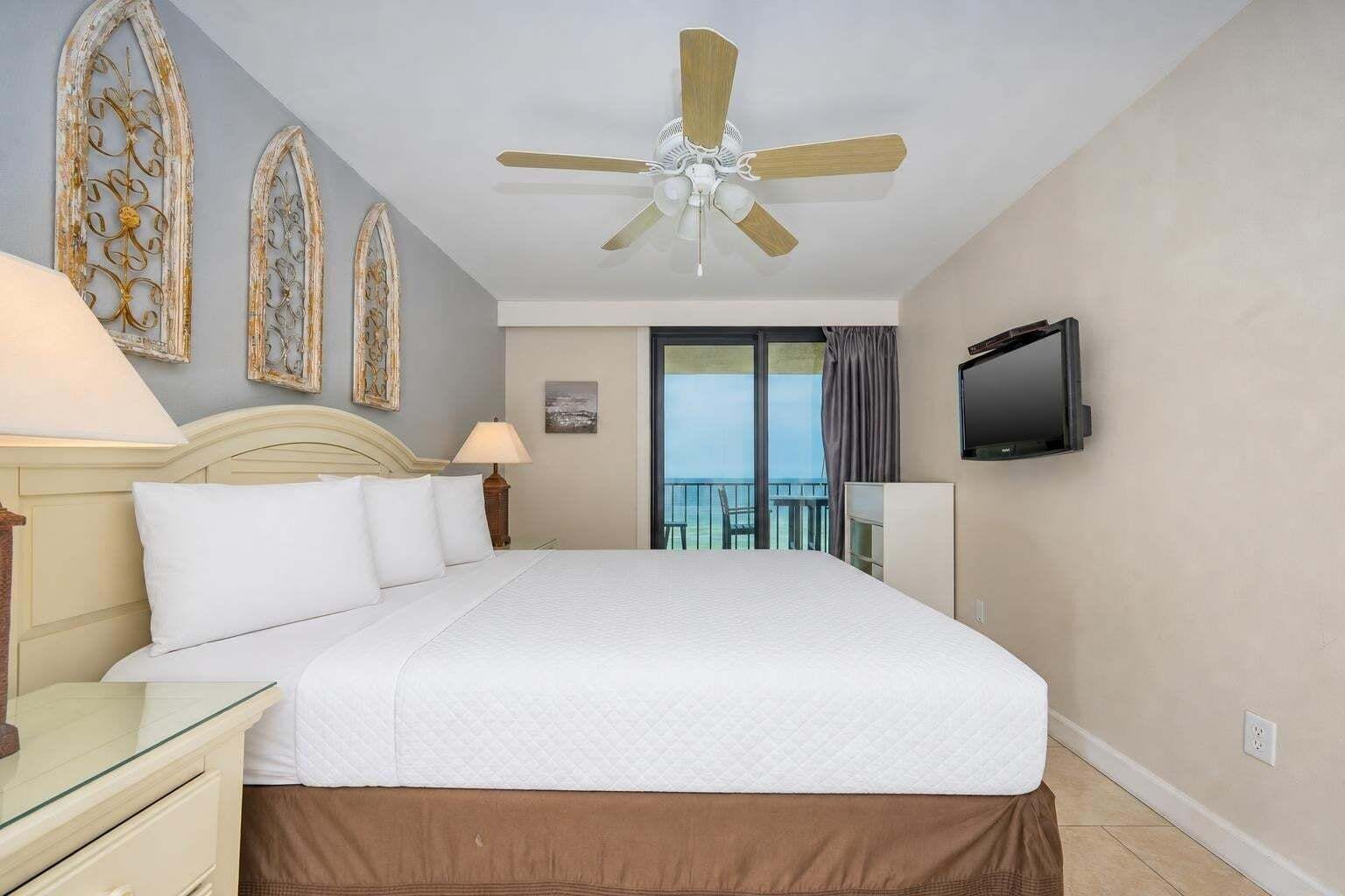 Une chambre d’hôtel avec un grand lit, un ventilateur de plafond, une télévision et un balcon avec vue.