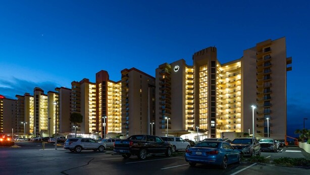 Ein mehrstöckiges Hotel mit beleuchteten Balkonen und einem Parkplatz voller Autos.