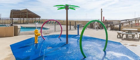 A water play area with a yellow fire hydrant, a green palm tree, and a red hoop.