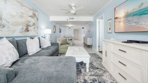 Ein Wohnzimmer mit grauem Sofa, einem weißen Couchtisch und einem großen Gemälde mit Strandmotiv.