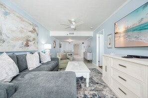 Ein Wohnzimmer mit grauem Sofa, einem weißen Couchtisch und einem großen Gemälde mit Strandmotiv.
