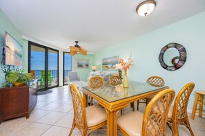 A dining area with a glass table and wicker chairs, a ceiling fan, and a view of the ocean through large sliding doors. - Phoenix Iii 3036 2 Bedroom Condo (Orange Beach)
