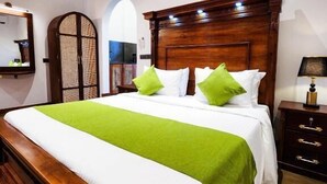 A hotel room with a wooden bed, green pillows, a nightstand, and a ceiling fan.