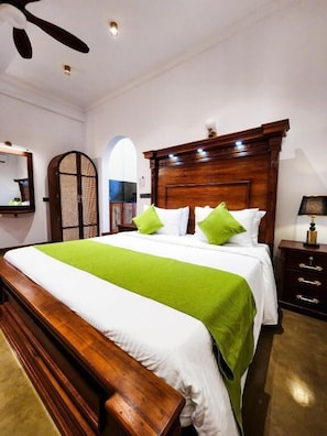 A hotel room with a wooden bed, green pillows, a nightstand, and a ceiling fan.