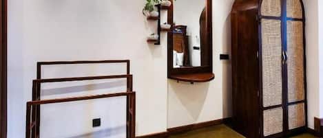 A hallway with a wooden floor, a wall-mounted light fixture, a mirror, and a door with a woven pattern.
