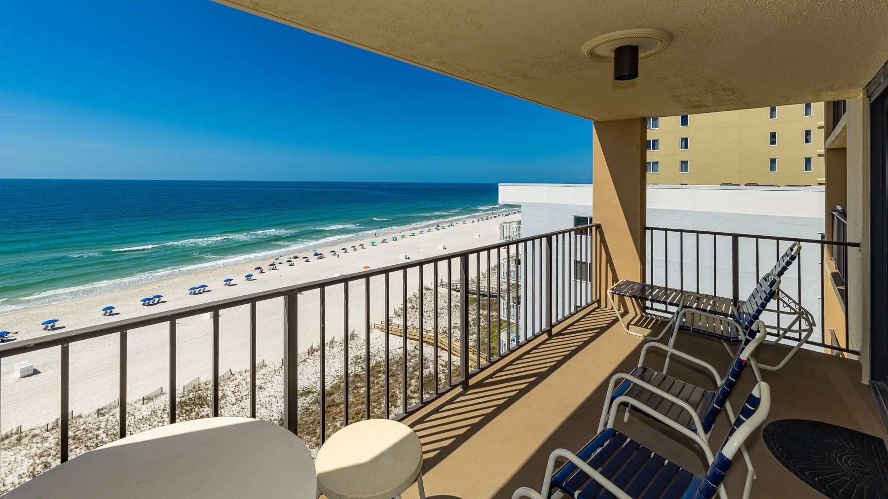 A balcony with a view of a beach and ocean, featuring a railing, a table, and two chairs.