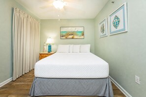 Une chambre à coucher avec un lit, une table de chevet, une lampe, un ventilateur de plafond et des œuvres d’art accrochées au mur.